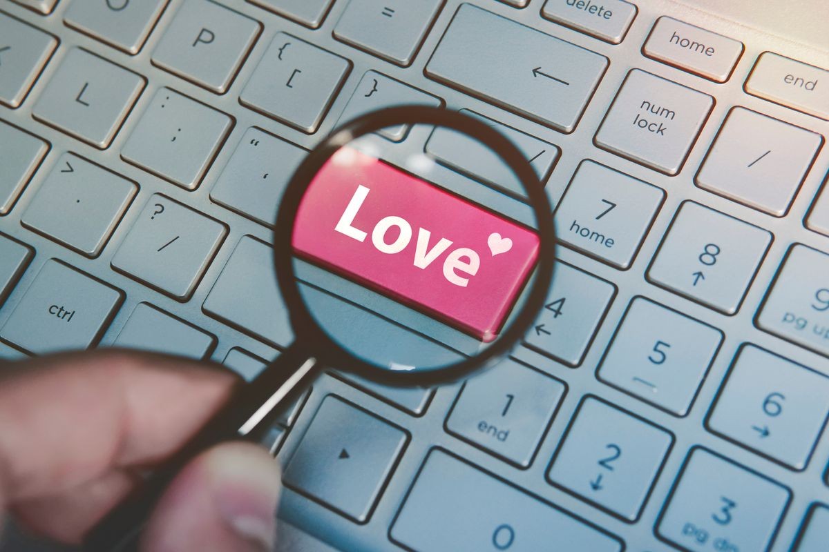 Written word love on keyboard red button viewed through the magnifying glass. Close up of male hand with loupe searching for love in internet. Concept of love search online. Dating services in net